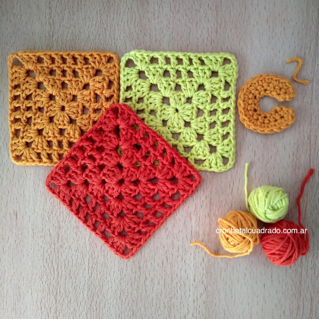 Tres cuadrados al crochet para principiantes en diferentes colores Tres cuadrados al crochet para principiantes tejidos en distintos colores apoyados sobre una mesa de madera