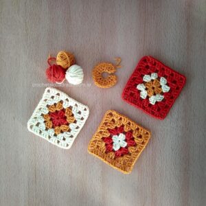 Cuadrado al crochet clásico con cambio de color tejido en vueltas Tres cuadrados al crochet clásico con cambio de color alineados sobre una mesa destacando la transición entre hileras