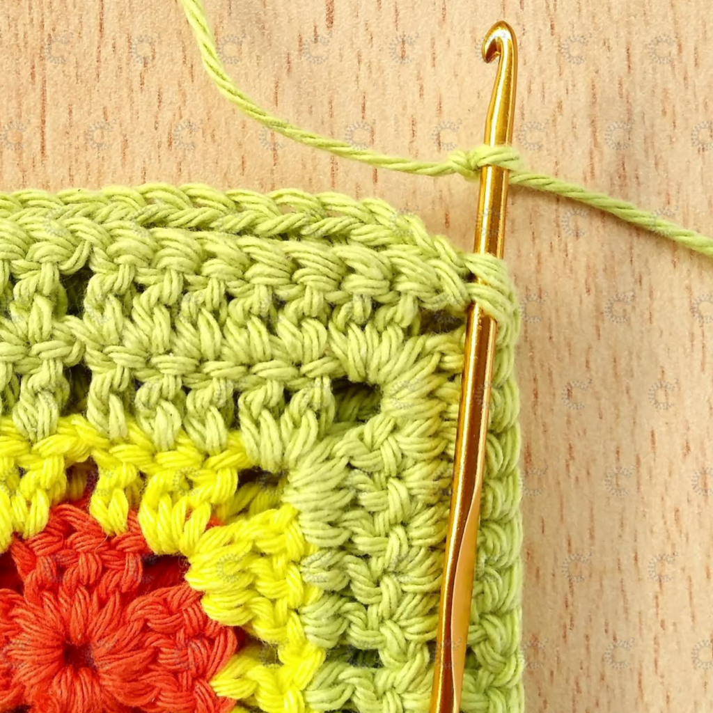 Aguja de crochet insertada en las lazadas externas de ambos cuadrados para comenzar la unión