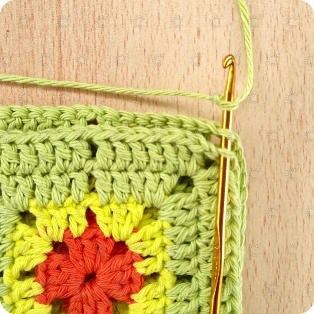 Aguja de crochet insertada en las lazadas internas del ángulo para comenzar la unión de cuadrados