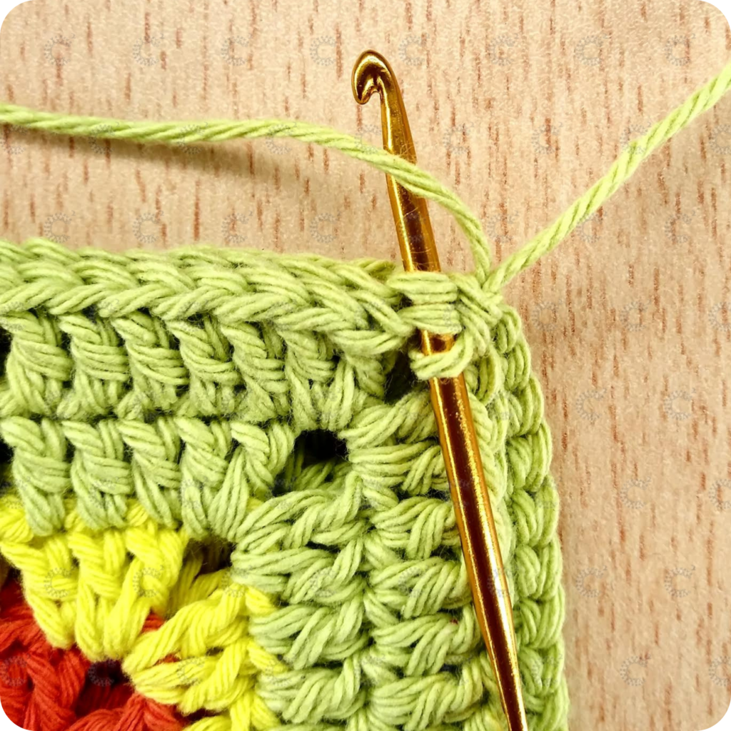 Aguja de crochet tomando las lazadas internas de ambos cuadrados para continuar la unión