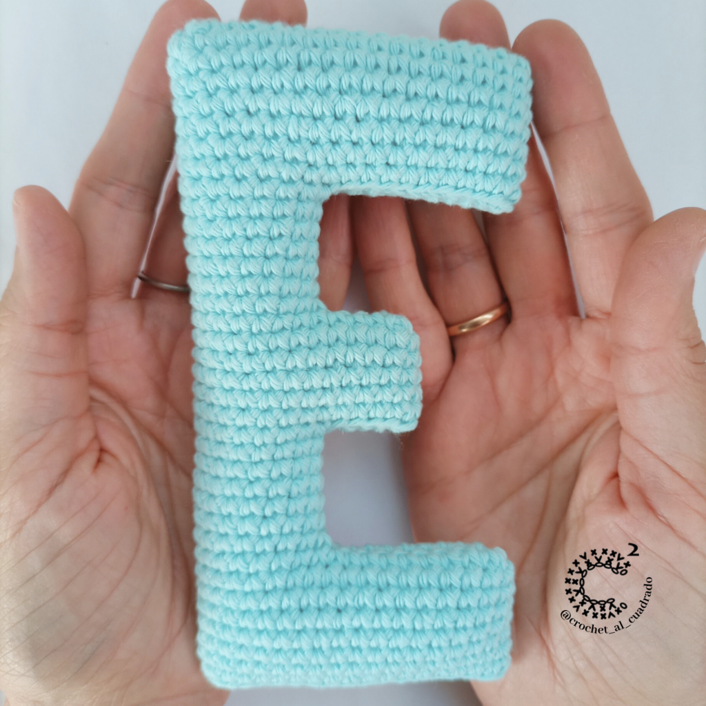 Manos sosteniendo la letra E amigurumi al crochet, letra tejida suave para alfabeto infantil